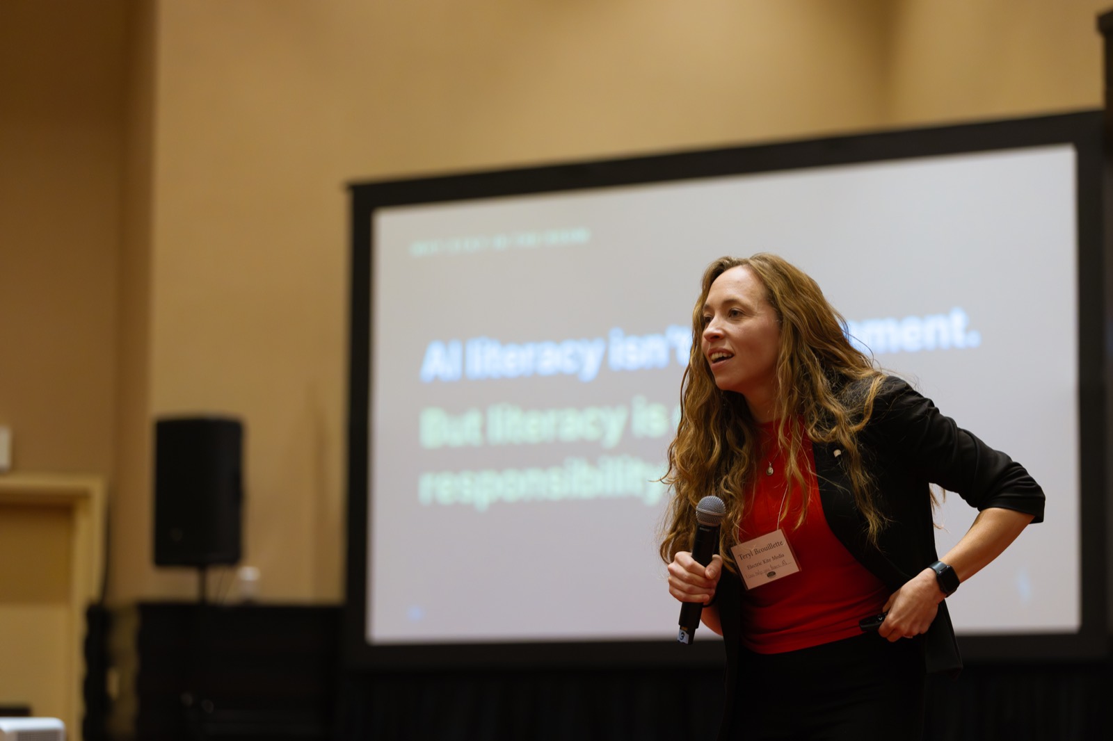 Teryl Brouillette on stage in front of a slide reading: AI literacy isn't endorsement. But literacy is our responsibility.