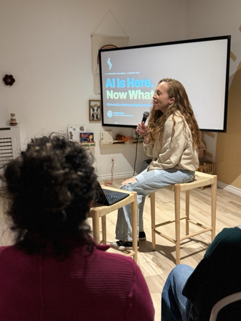 Teryl Brouillette seated with a microphone beside the AI Is Here. Now What? title slide